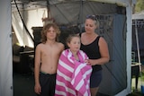 A woman and two children stand posing for a photo in front of a gazebo in a caravan park.