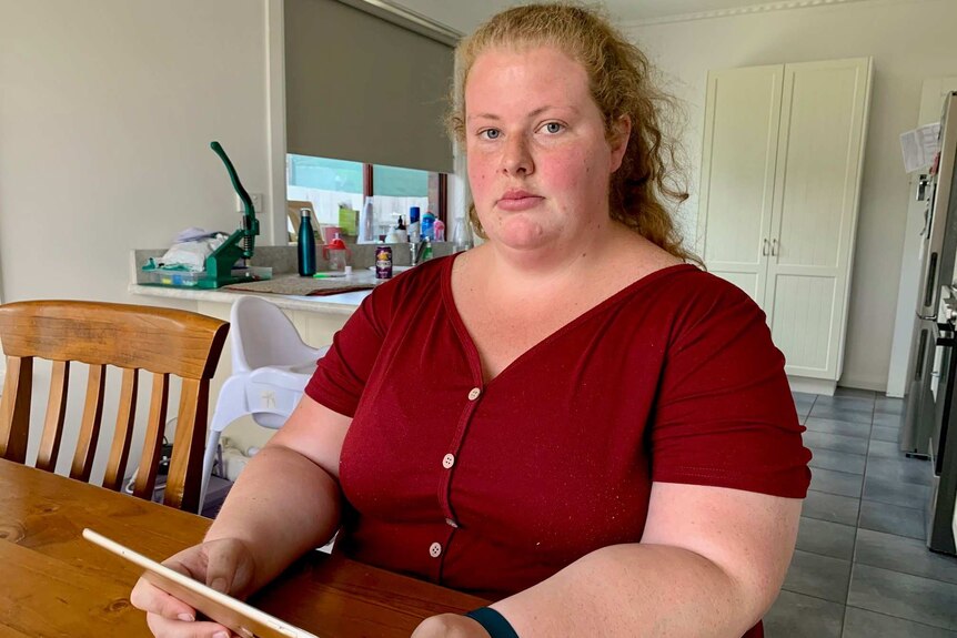 Sexual abuse survivor Keelie McMahon sits in her kitchen holding an iPad.