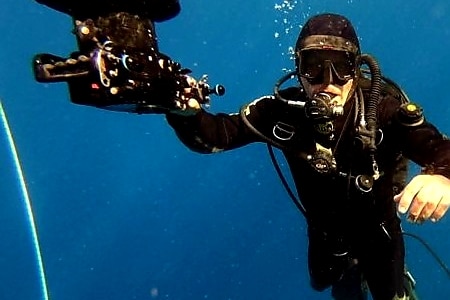 A man in a wet suit is underwater looking at the camera