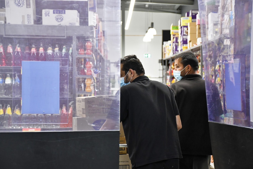 Two men wheel a trolley full of food, ready to stock shelves.