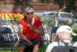 Pat Ansell Dodds sits on a chair and speaks into a microphone at an Invasion Day rally in Alice Springs