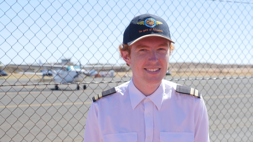 A young pilot stands in front of a Cessna plane.