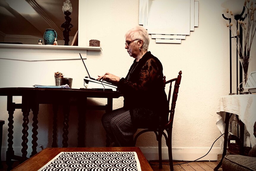 Woman sits at a desk, typing on a laptop