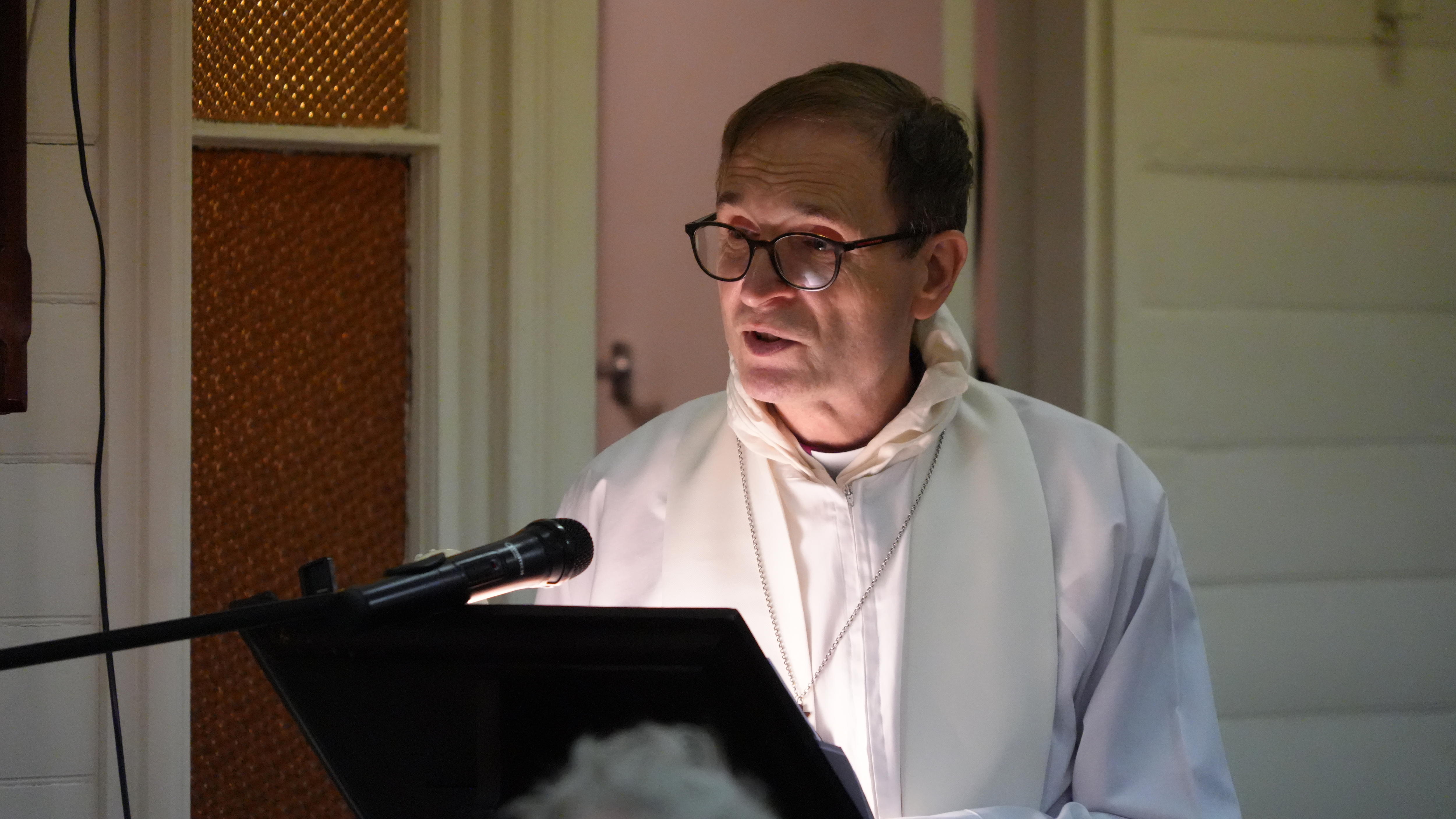 A man wearing bishop's robes speaks into microphone 