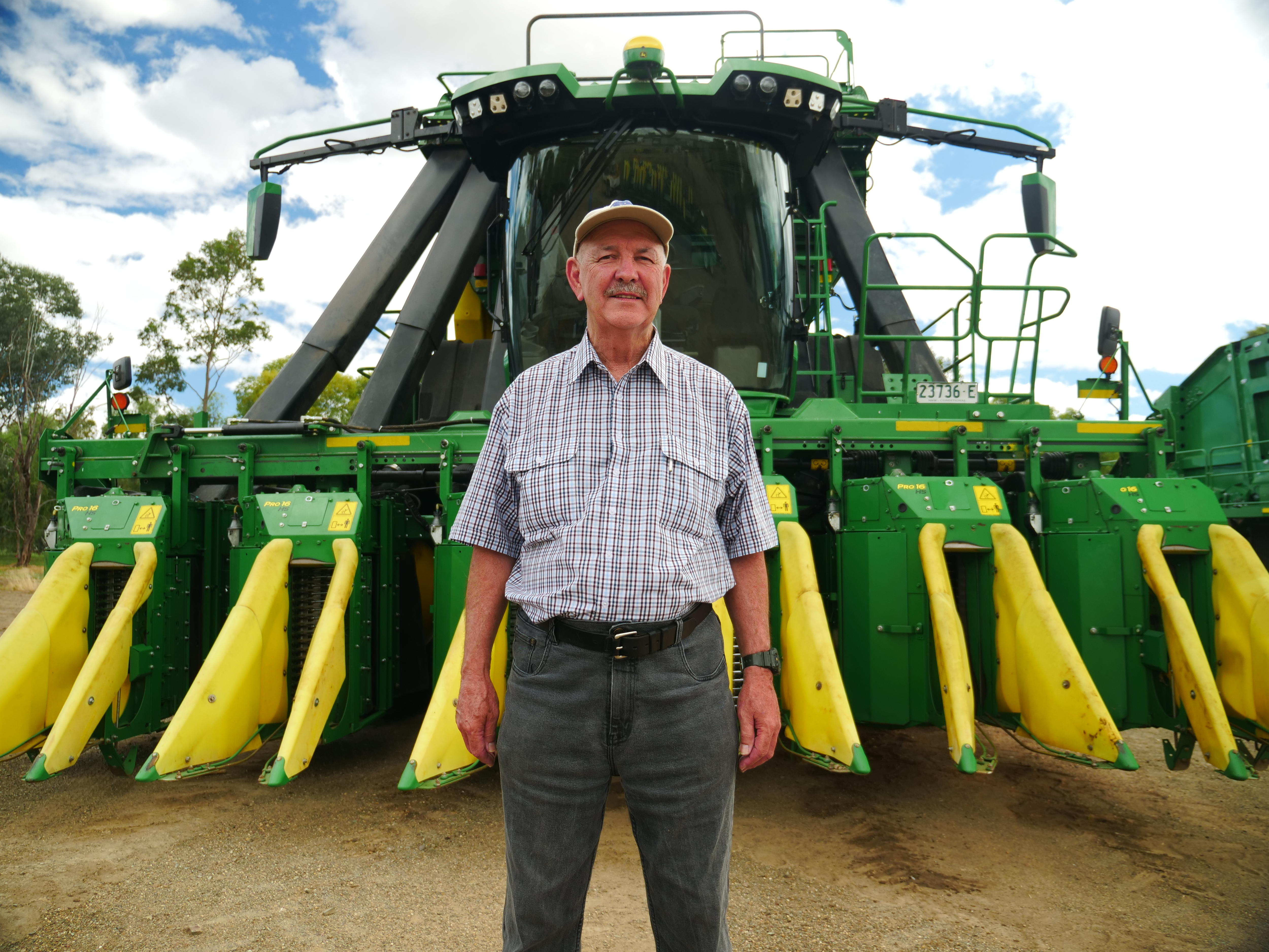 Man stands in front of cotton picker machine.