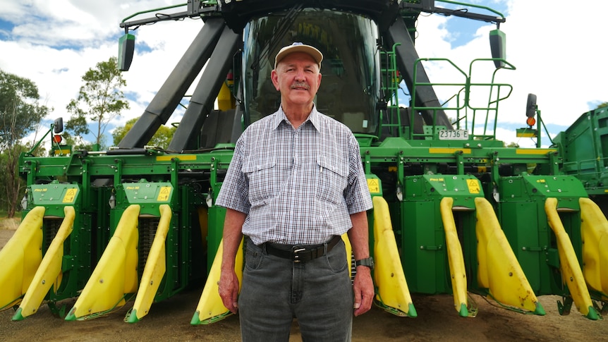 Man stands in front of cotton-picking machine.