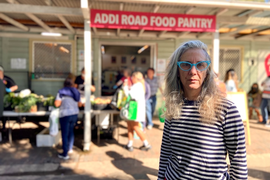 A woman in glasses and a striped shirt stands outside a shop