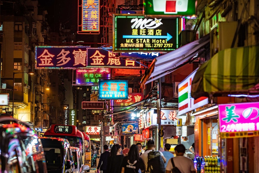 Hong Kong street at night. People walk along a busy street, above them are a number of neon signs.