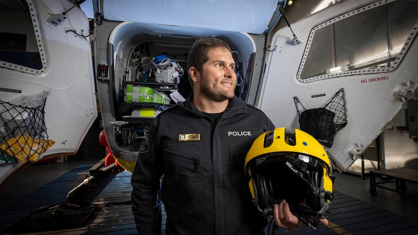 Police officer holding a helmet, standing in front of a helicopter with the doors open