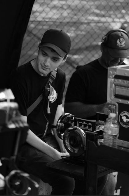 A black and white photo of Sam Riesel on set with cameras and other equipment