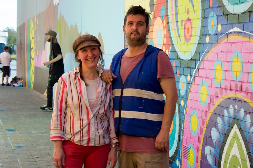 A woman and a man stand in a brightly painted laneway.