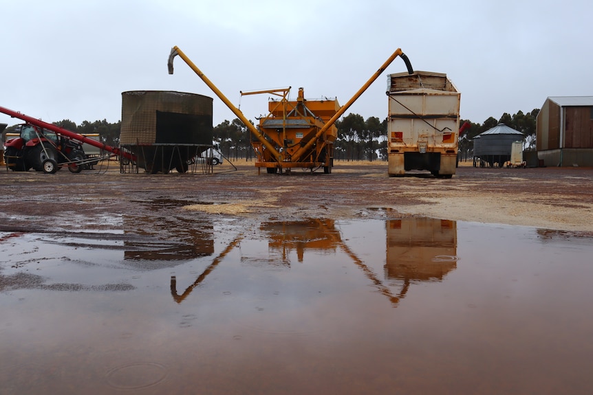 Farm equipment in a yard with large puddles in it.