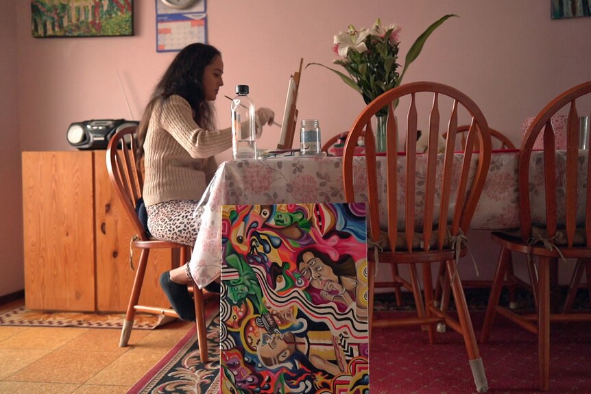 A woman sits at a dining table painting.