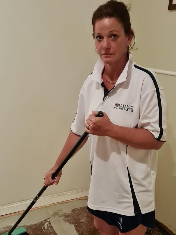 A woman looking exhausted mops up water off the floor.