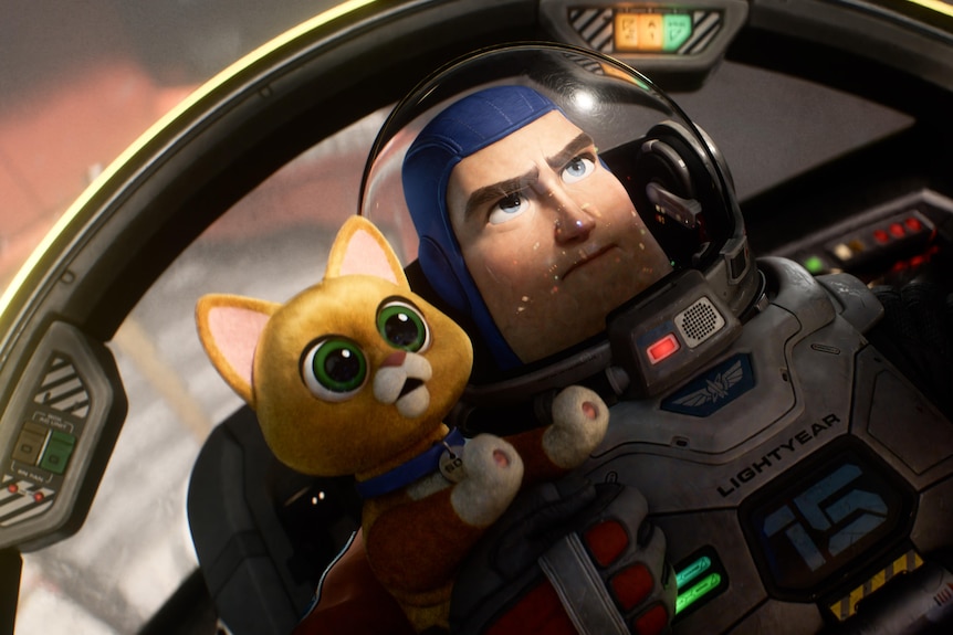 A live orange cat with green eyes lives next to a person in a space suit and foam hat inside the space shuttle.