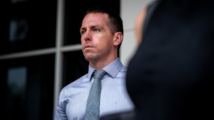 a young man wearing a blue collared shirt outside court