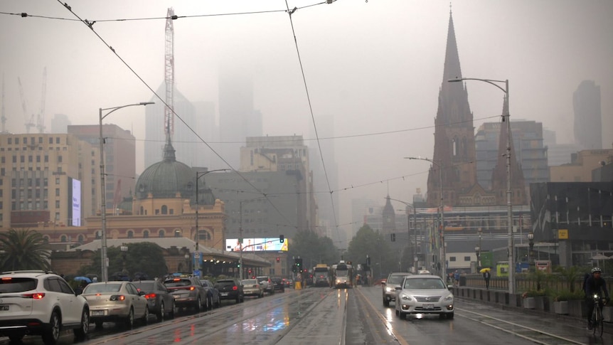 Cars drive over Princes Bridge in Melbourne towards Flinders Street Station and the CBD which are shrouded in a grey haze.