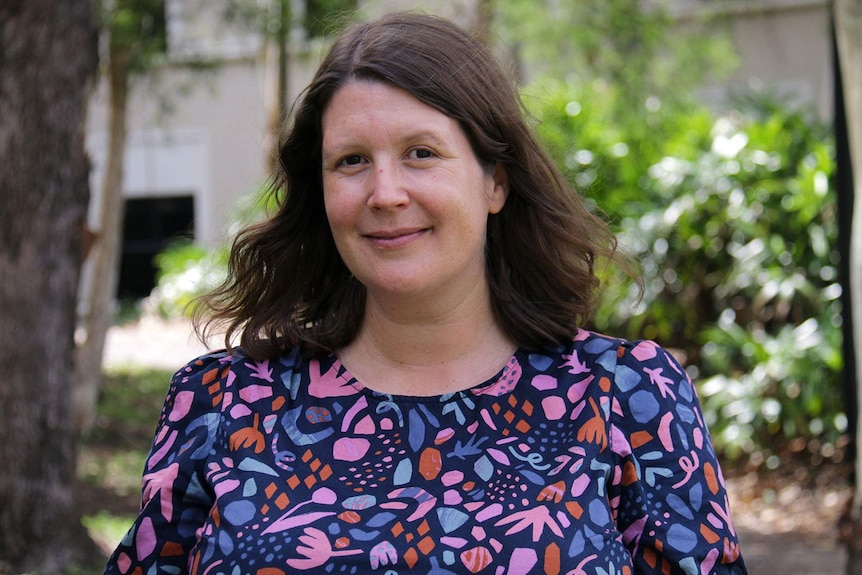 A woman smiling standing in a wooded outdoor area