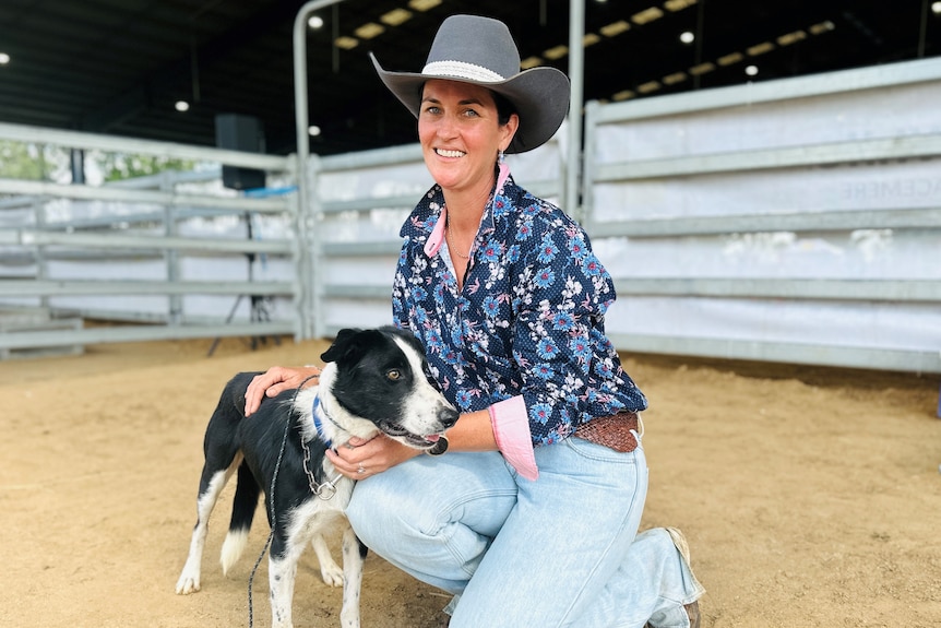 A woman wearing an Akubra hat, dark shirt and jeans with a black and white border collie dog.