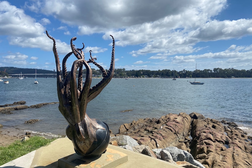 A squid sculpture by the water with boats in the background.