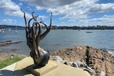 A squid sculpture by the water with boats in the background.