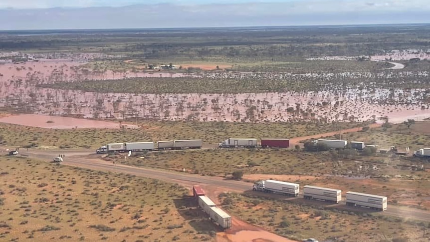 An aerial photo of a waterlogged outback setting showing b-double and triple road trains parked on and off the road.