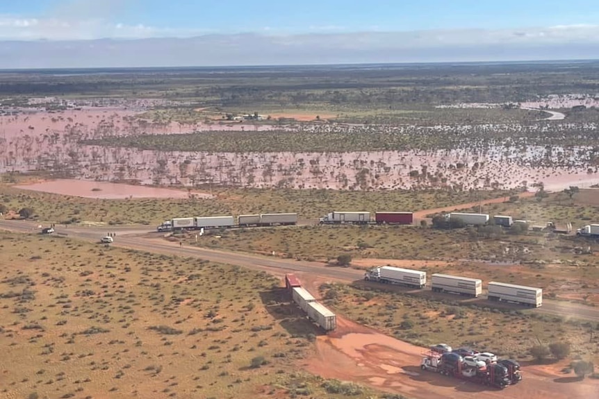 An aerial photo of a water-filled outback setting showing b-double and triple-carriages parked on and off the road.