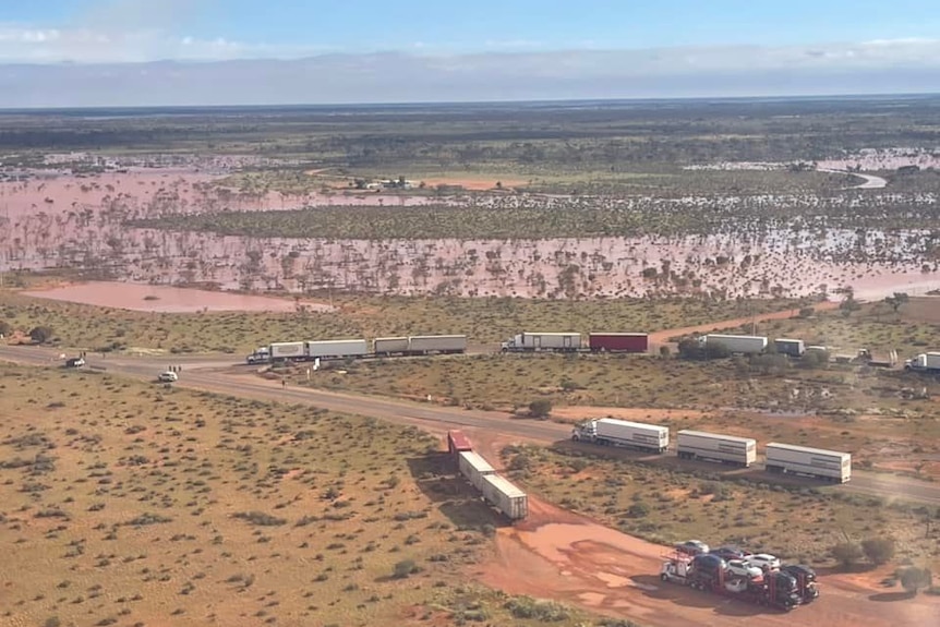 An aerial photo of a waterlogged outback setting showing b-double and triple road trains parked on and off the road.