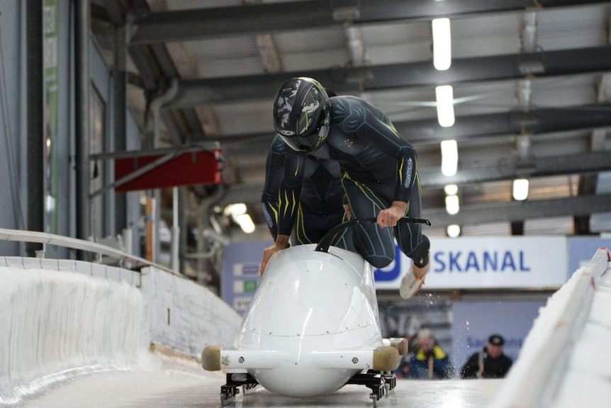 Two riders jump into bobsleigh wearing lycra speed suits