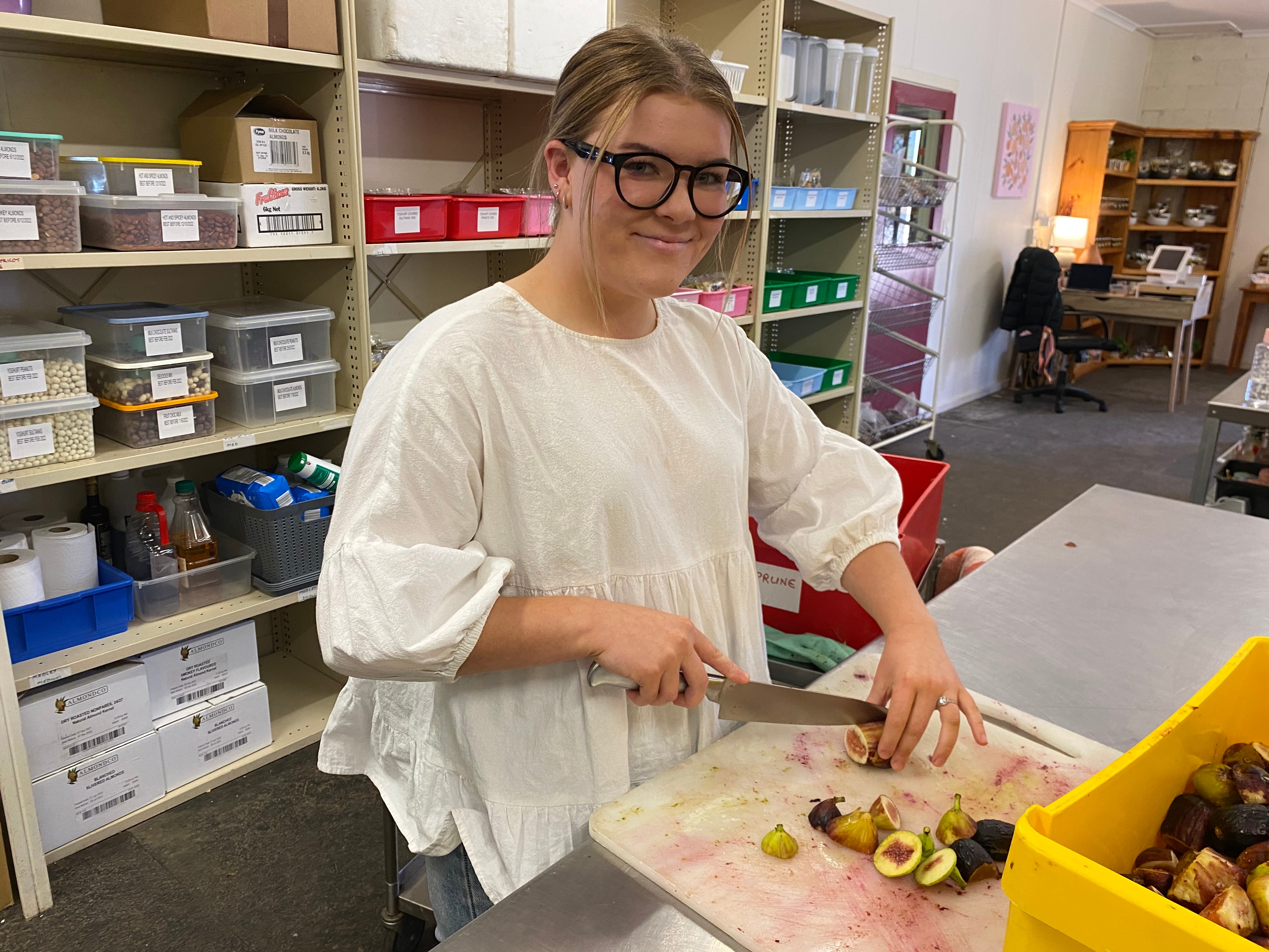 Woman chops fruit at a bench.