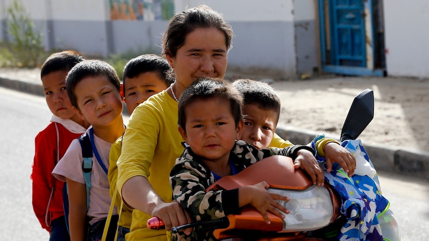 A Uyghur woman and children sit on a motor-tricycle after school.