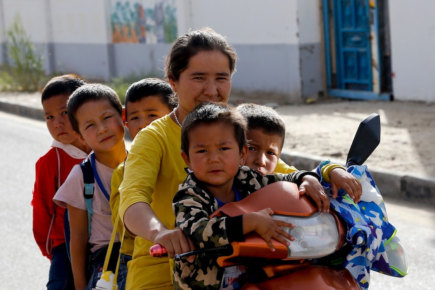 A Uyghur woman and children sit on a motor-tricycle after school.