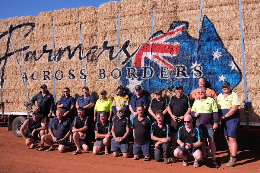 People standing in front of truck with hay on the back and Farmers Across Boarders logo.