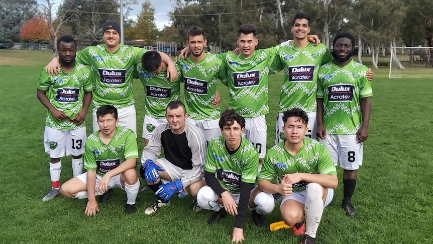 A group of men wearing identical football kits pose on a field for a photo.