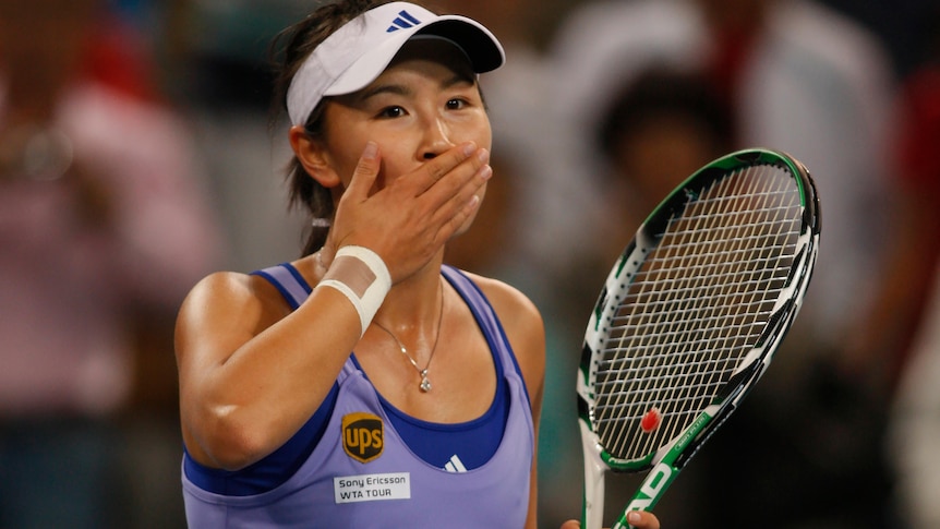 A photo of Peng Shuai in tennis match with her hand over her mouth.