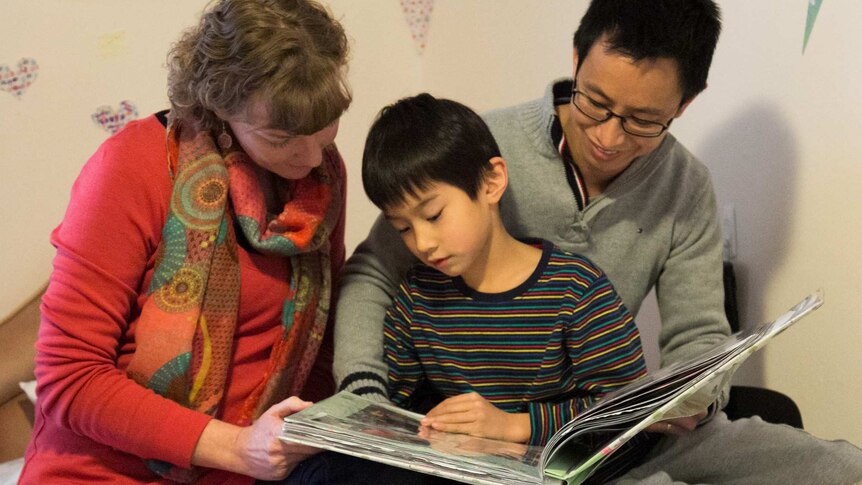 Naomi, Aaron and Lucas Cheang look through a family scrapbook