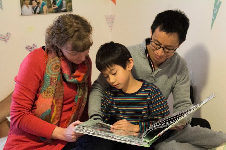 Naomi, Aaron and Lucas Cheang look through a family scrapbook