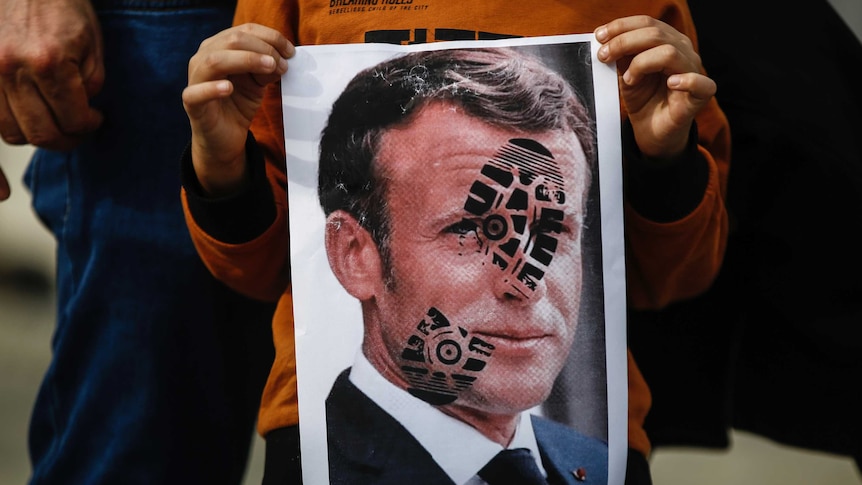 A child holds an image of Mr Macron with a shoe print on his face.