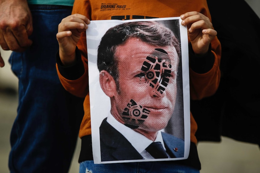 A child holds an image of Mr Macron with a shoe print on his face.