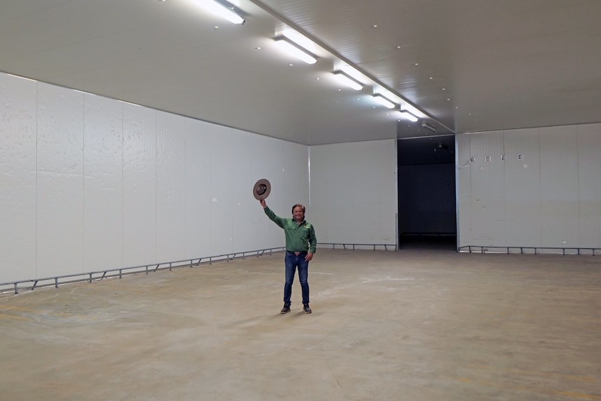 A man waving his hat inside a massive freezer room.