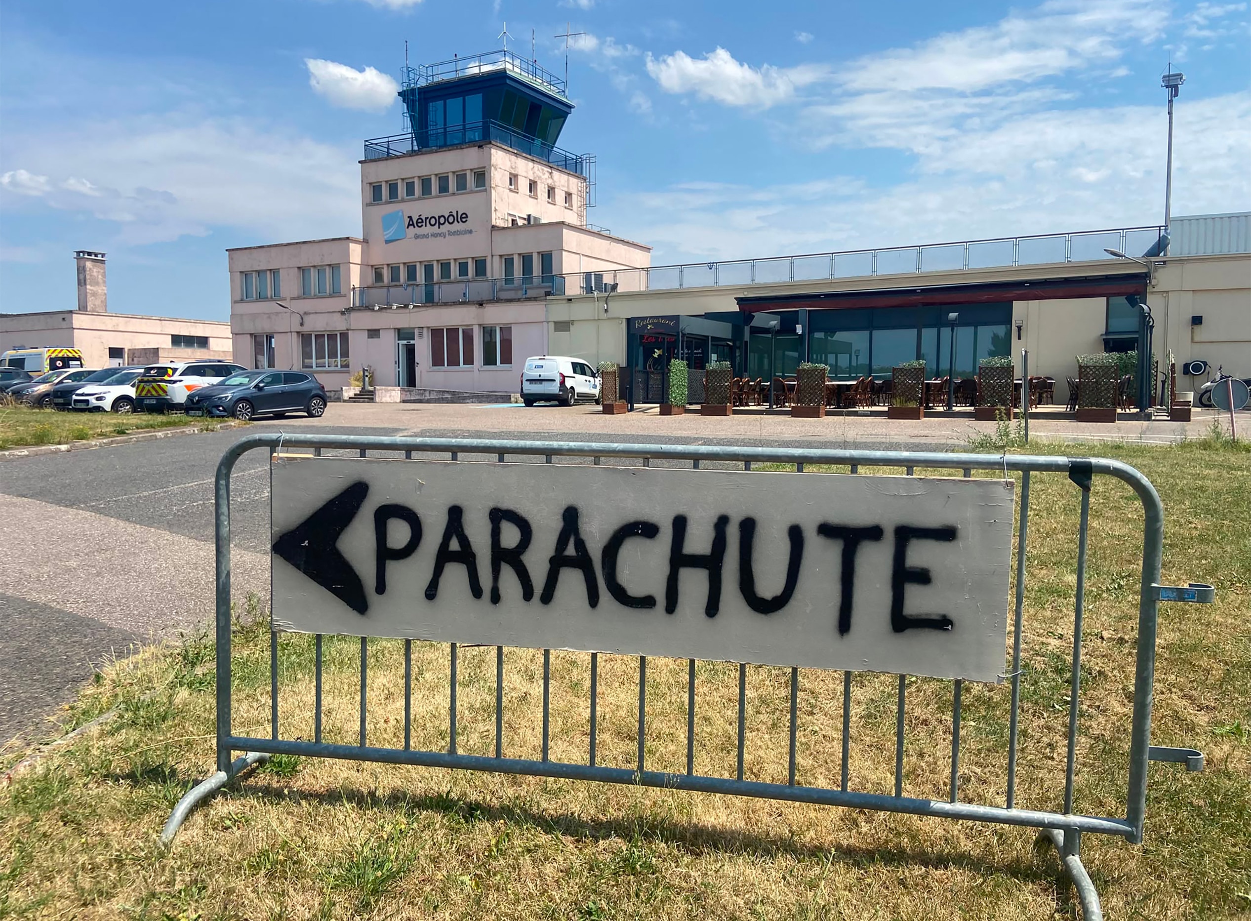 A aerodrome with a hand-written sign on a fence saying PARACHUTE