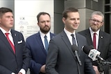 Four men in suits speaking at a press conference