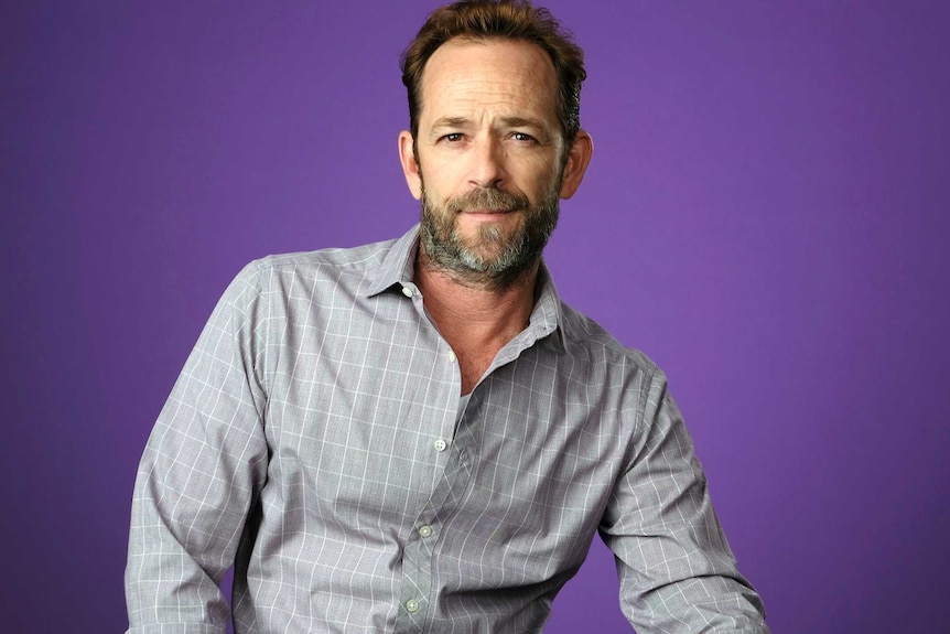 Actor Luke Perry sits on a chair.