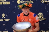 Australian surfer Stephanie Gilmore wears a garland of flowers and shouts with joy while holding a trophy after winning a title.