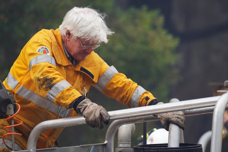 A firefighter with white hair leans over the front of a vehicle