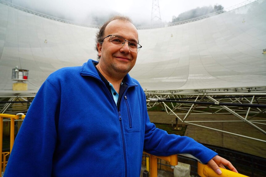 CSIRO astrophysicist George Hobbs looks at camera with FAST radio telescope behind him