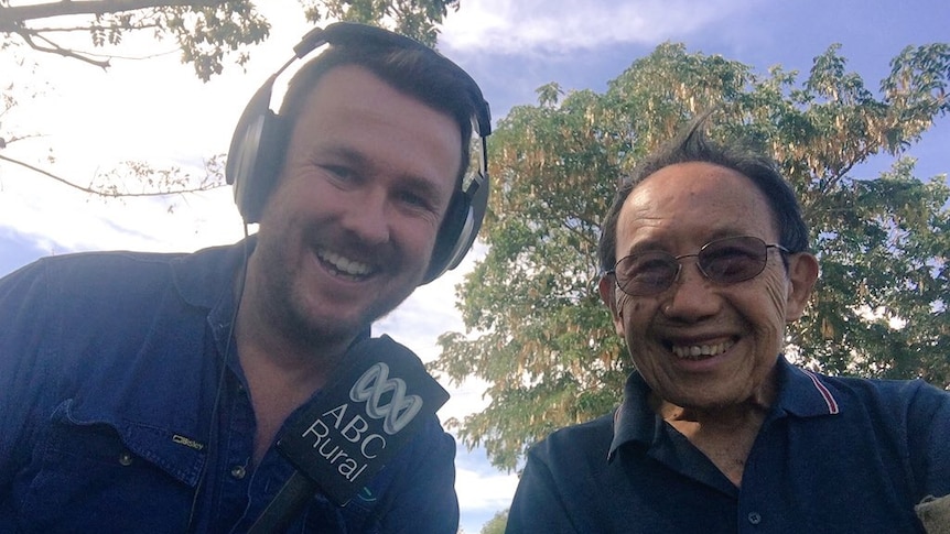 two men, one with a set of headphones on with a tree in the background.