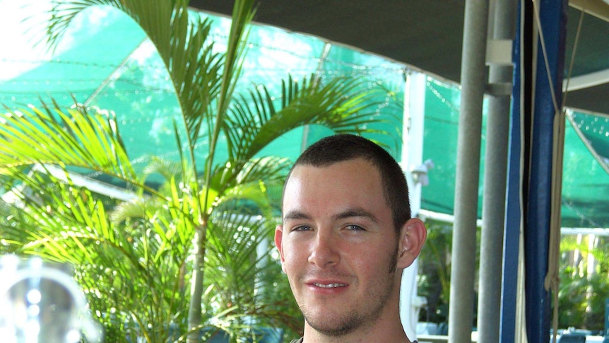 A smiling man with short hair wearing a green shirt sitting in a garden.