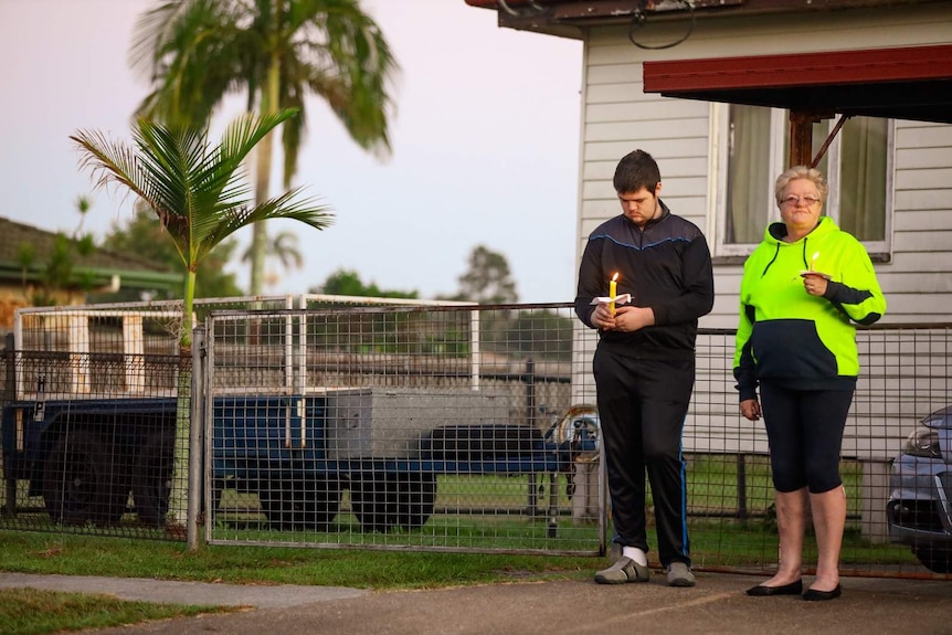 A young man and a woman holding candles on the driveway of a suburban house