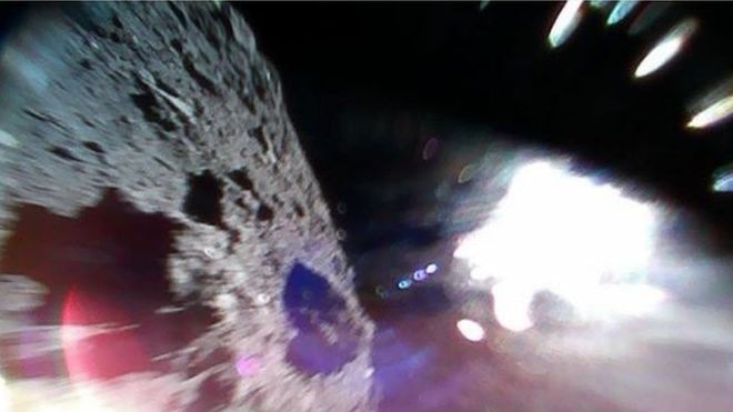 Picture shows the surface of the asteroid on the left and a white sun glare on the right